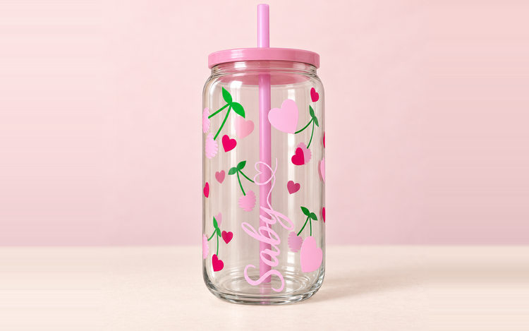 Vaso de cristal personalizado con corazones, tapa y pajita rosas sobre fondo pastel